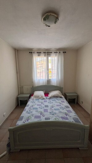 A bedroom with a single bed, a window with curtains, a bedside table, and a nightstand. - Cozy apartment with a view of the Paillon garden (Nice)
