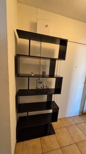 A black, multi-tiered shelving unit against a wall with a tiled floor. - Cozy apartment with a view of the Paillon garden (Nice)