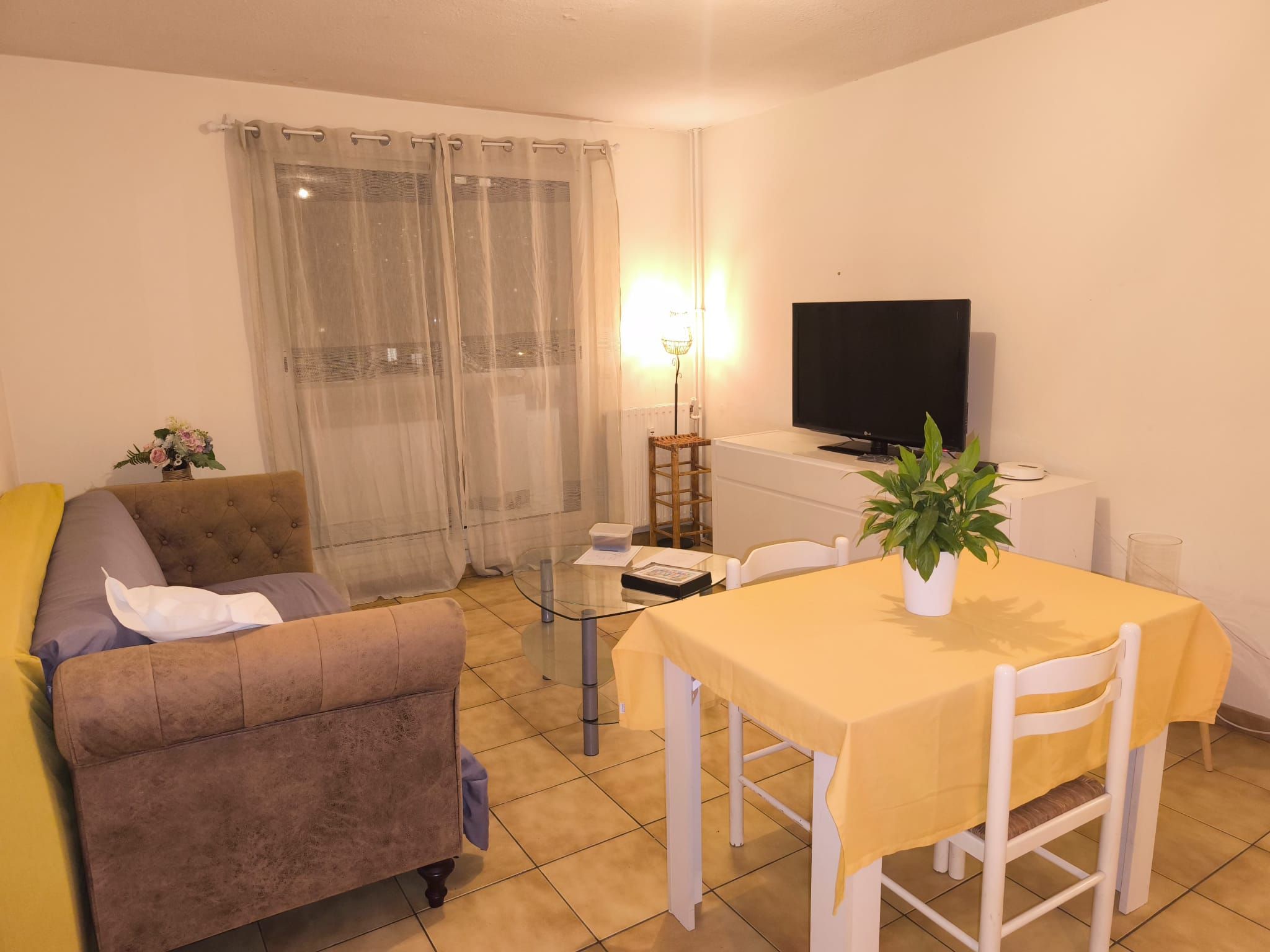 A living room with a sofa, a glass coffee table, a TV, and a dining table with chairs.