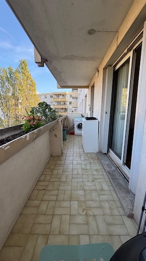 A balcony with a washing machine, a trash bin, and a planter with plants. - Cozy apartment with a view of the Paillon garden (Nice)