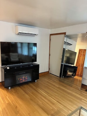 Una sala de estar moderna con una televisión de pantalla plana, una chimenea y una cocina visible a través de un separador de vidrio.