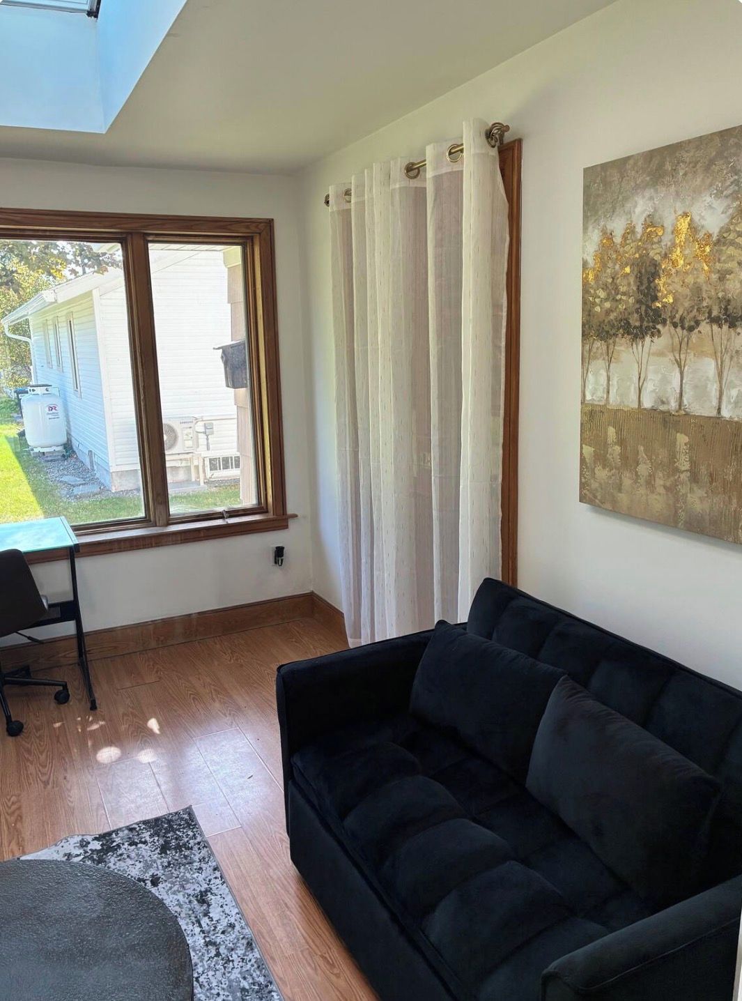 A living room with a black sofa, a painting on the wall, and a window with curtains.