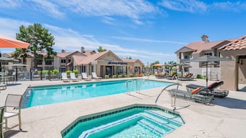 Une piscine dotée de chaises longues et d’un jacuzzi, entourée de maisons, avec un ciel dégagé.