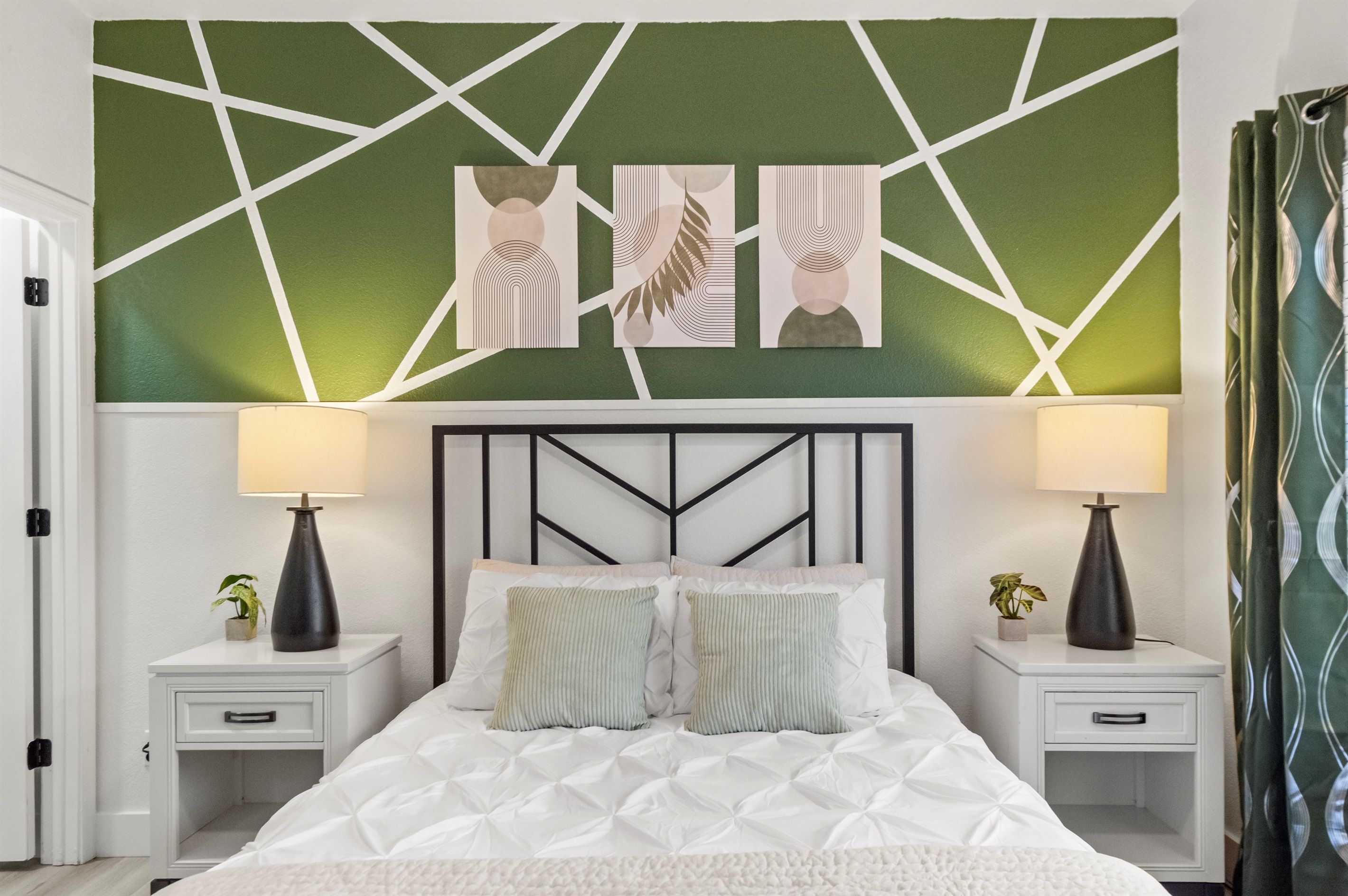 Un lit avec une tête de lit aux motifs géométriques, deux tables de chevet avec des lampes et des œuvres d’art accrochées au mur.