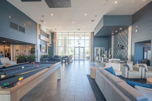 Eine moderne Hotelhalle mit Billardtisch, bequemen Sitzgelegenheiten und einer großen Glasdoor, die nach draußen führt.