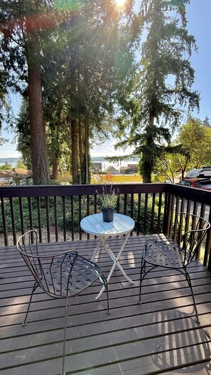 Eine Holzterrasse mit einem runden Tisch und zwei Stühlen, mit Blick auf ein Wohngebiet mit Häusern und einem Gewässer.