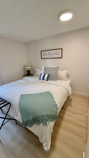 Ein Schlafzimmer mit einem Bett, Kissen, einer Nachttischlampe, einem gerahmten Schild an der Wand und einer grünen Tagesdecke.