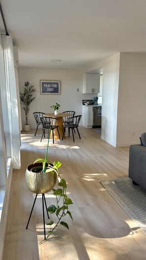 A modern living space with a dining area, kitchen, and a large window providing natural light. - Twin Tides South | Renovated 2BR (Bremerton)