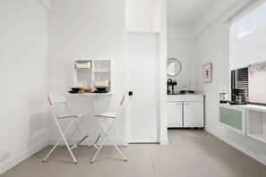A modern kitchen with white cabinetry, a dining area with two chairs, and a coffee machine. - San Rafael Apt 6 | Cozy 1 BR Retreat @ San Juan (San Juan de Puerto Rico)
