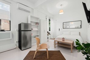 A modern bedroom with a bed, a bedside table, a chair, a refrigerator, and a wardrobe. - San Rafael Apt 6 | Cozy 1 BR Retreat @ San Juan (San Juan de Puerto Rico)