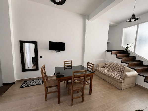 A modern living space with a dining area, sofa, staircase, and a TV mounted on the wall. - Cozy 1-bedroom apartment in peaceful Mercedes with AC (Mercedes)