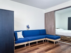 A modern room with a blue sectional sofa, wooden flooring, and a large mirror. - HANASTAY IMAZATO TOGEN (Osaka)