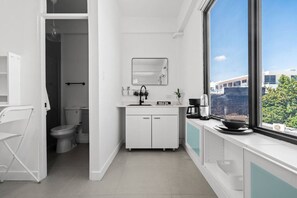 A modern bathroom with a toilet, sink, and mirror. There is a window providing a view of buildings outside. - San Rafael Apt 7 | Chic Comfort Place @San Juan (San Juan de Puerto Rico)