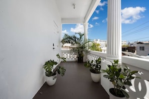 A balcony with white columns, potted plants, and a clear view of buildings in the background. - San Rafael Apt 7 | Chic Comfort Place @San Juan (San Juan de Puerto Rico)