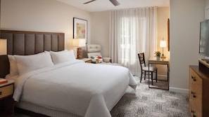Quarto de hotel com uma cama grande, uma escrivaninha, uma cadeira, uma televisão e um ventilador de teto.