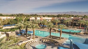Um resort com várias piscinas, palmeiras e montanhas ao fundo.