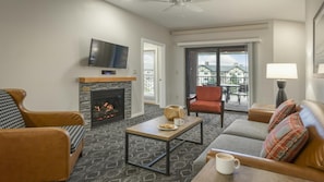 A living room with a fireplace, a television, a sofa, a coffee table, and a balcony with a view.