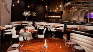 L’intérieur d’un restaurant avec des tables rondes, des chaises blanches et une cheminée centrale.