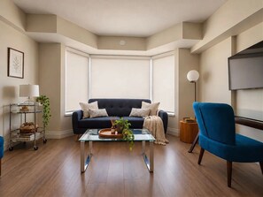 A modern living room with a dark blue sofa, a glass coffee table, and a blue armchair. - Skyline 2BR Suite in Yorkville • 2 Baths & Kitchen (Toronto)