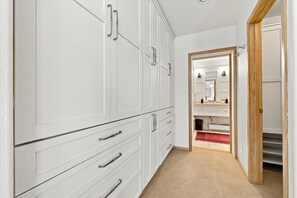 Ein Flur mit weißen Schränken, einer Holztür und einem Spiegel, der ein Badezimmer mit einer roten Teppich zeigt.