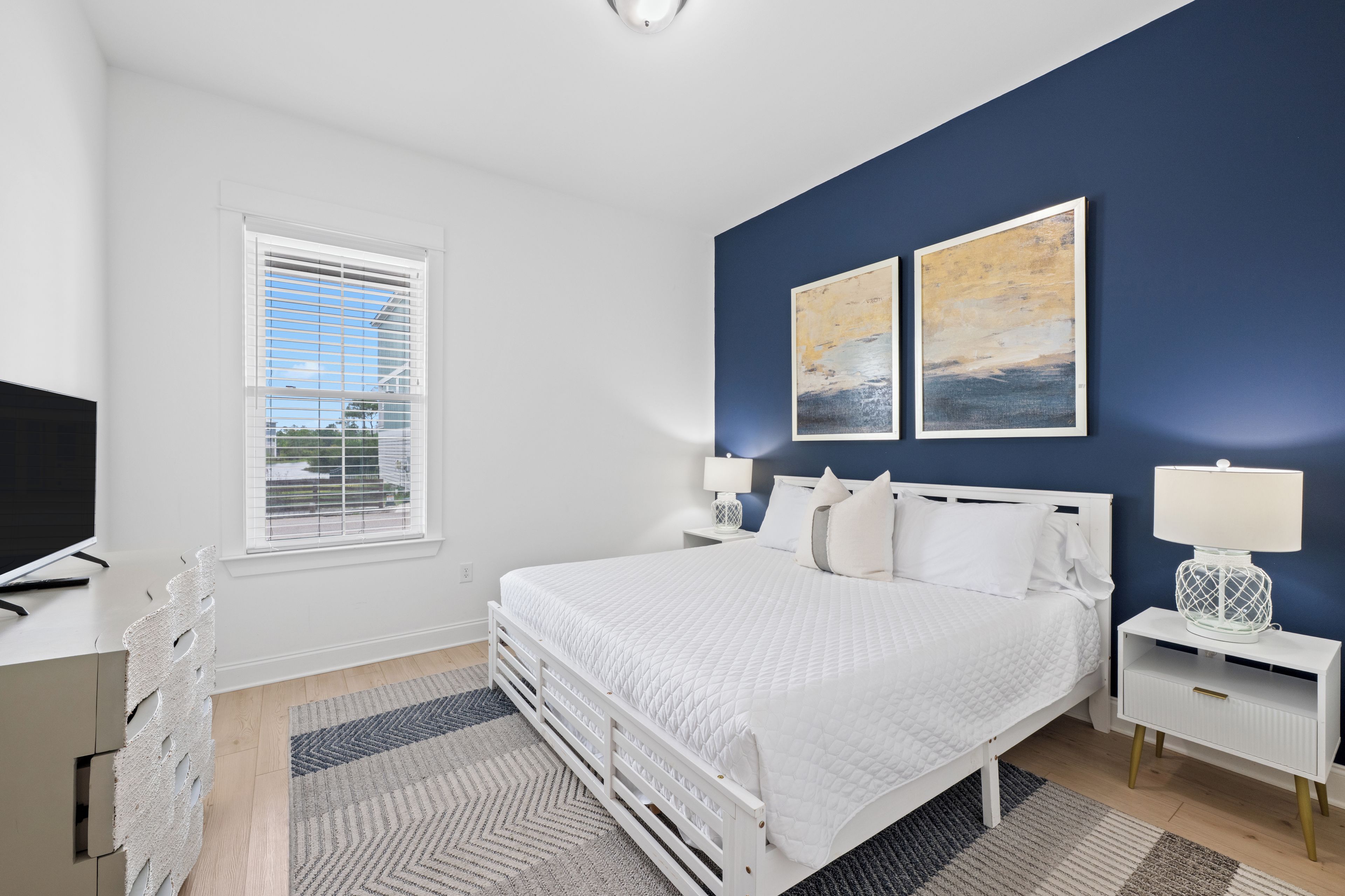 A bedroom with a bed, bedside tables, a TV, and artwork on the wall.
