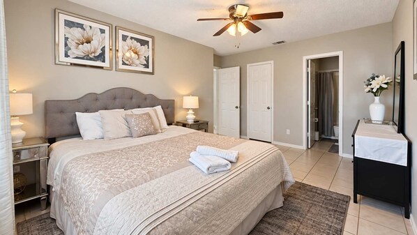 A bedroom with a bed, bedside lamps, a ceiling fan, and framed floral artwork on the wall. - ATX Basecamp - Near The Domain & Q2 Stadium (Austin)