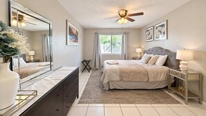 A bedroom with a bed, bedside tables, a mirror, a ceiling fan, and a window with curtains. - ATX Basecamp - Near The Domain & Q2 Stadium (Austin)