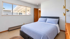 Une chambre à coucher avec un lit, une fenêtre, un radiateur et une commode en bois.