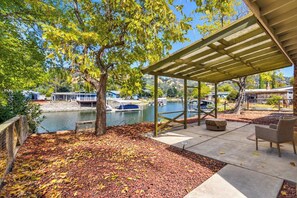 Un patio abrité avec vue sur un lac et des bateaux, entouré d’arbres et d’un mur de pierre.
