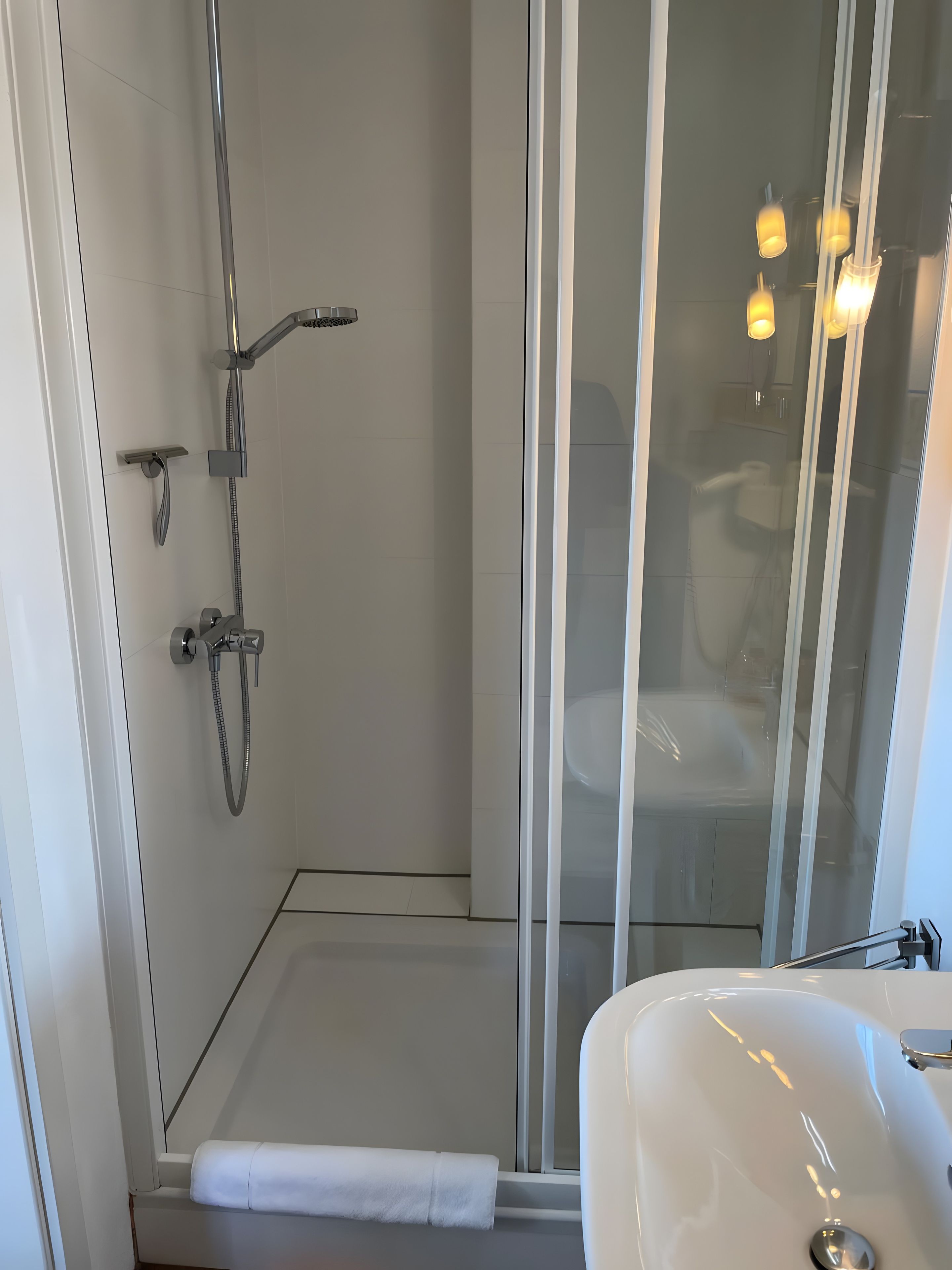 A modern bathroom with a glass-enclosed shower, a white sink, and a towel rack.