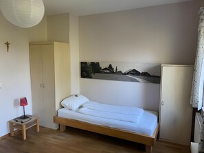 A single bed with a wooden frame, a small bedside table with a lamp, a wardrobe, and a wall-mounted picture. - Studio Apartment 'Marleen' with Wi-Fi (Ottobeuren)