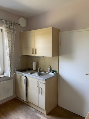 Eine kleine Küche mit Backofen, Spüle und einem Fenster mit Vorhängen.