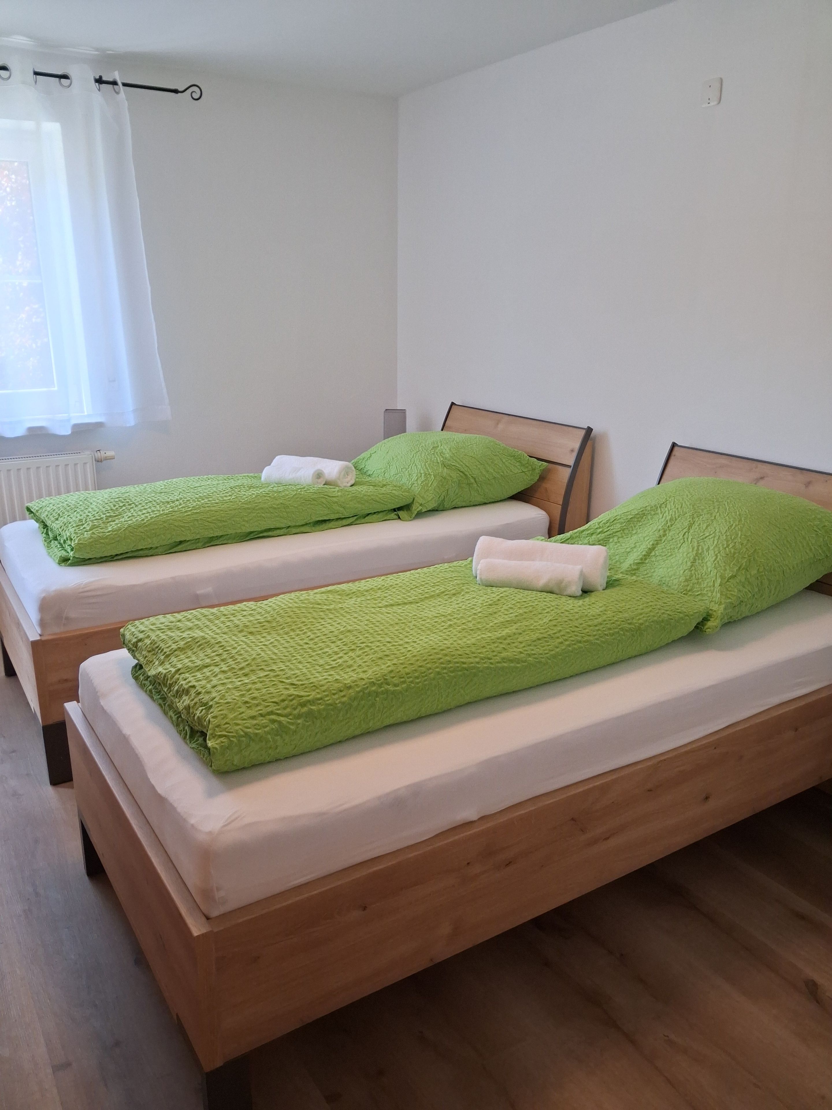 Una habitación con dos camas de madera, cada una con una manta verde y almohadas blancas.