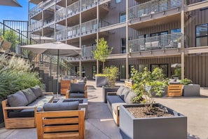 An outdoor seating area with modern furniture, surrounded by a multi-story building with balconies. - Bluebird By Broadway in Downtown Nash & Enjoy Pool, Gym, Parking. Walk to Broadway! (Nashville)