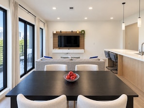 A modern kitchen with a dining area, a flat-screen TV mounted above the counter, and a bowl of apples on the table. - Bluebird By Broadway in Downtown Nash & Enjoy Pool, Gym, Parking. Walk to Broadway! (Nashville)