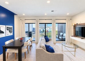 A modern living room with a sofa, dining table, and chairs. There is a television on a stand and a window with curtains. - Bluebird By Broadway in Downtown Nash & Enjoy Pool, Gym, Parking. Walk to Broadway! (Nashville)