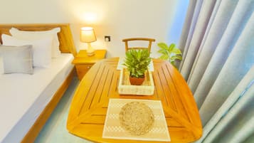 Una habitación de hotel con una cama, una mesita de noche con lámpara, una mesa de madera con una planta y un adorno en la pared.