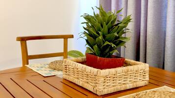 Une table de salle à manger en bois, surmontée d’un set de table en fibres tressées, un autre set de table en fibres tressées posé sur le sol, un panier tressé et une plante en pot.