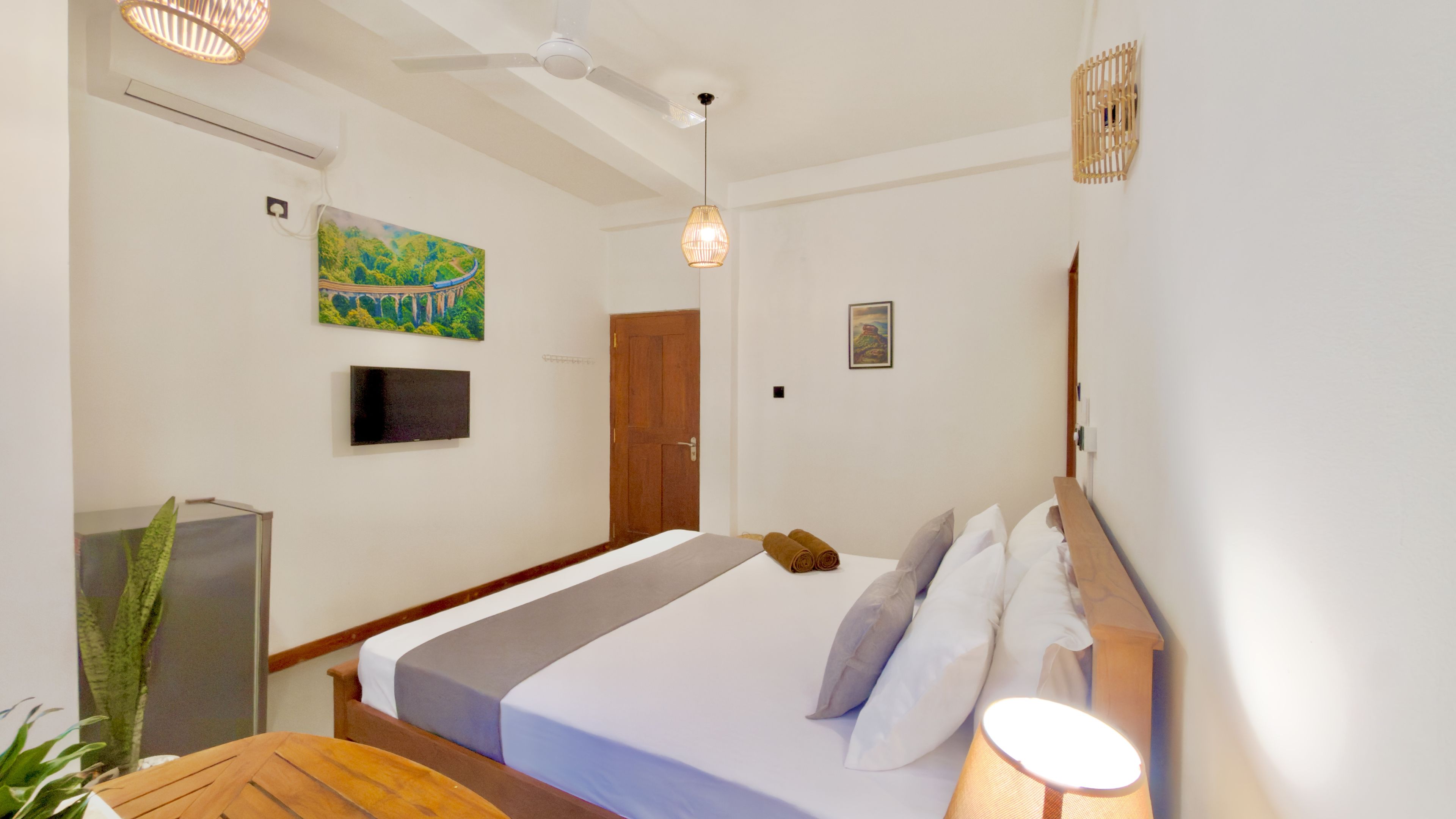 Une chambre d’hôtel avec un lit, une télévision, un ventilateur de plafond, un tableau et une porte.