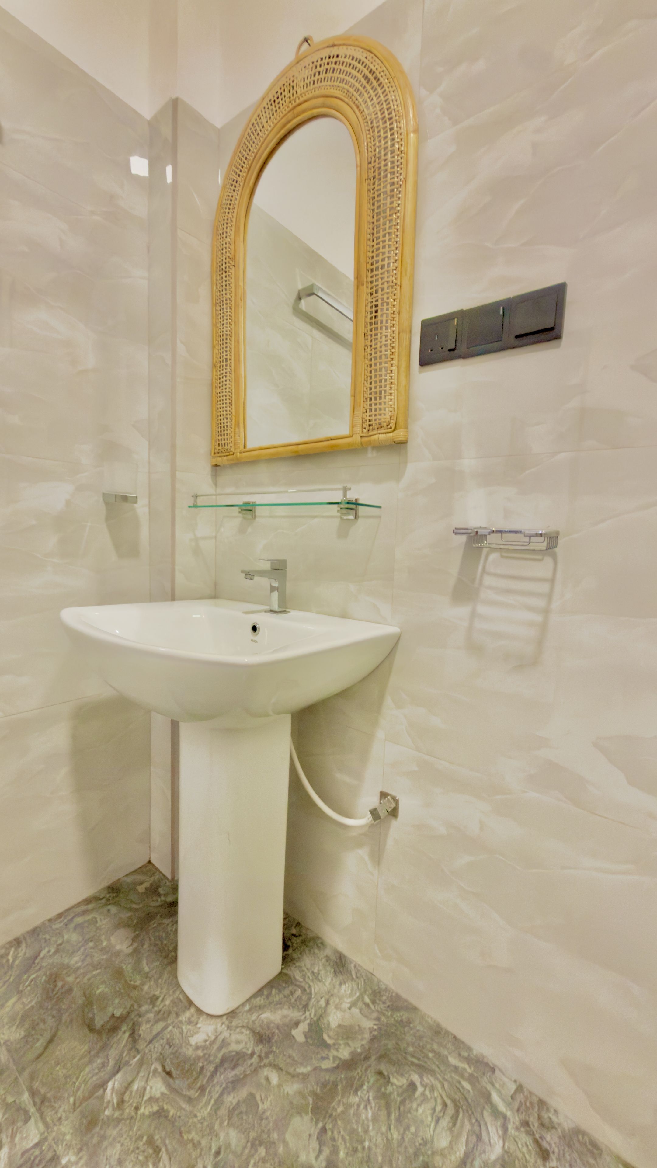 A bathroom with a white pedestal sink, a mirror with a woven frame, and a towel rack.