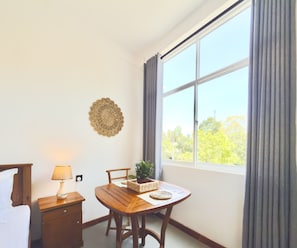 A room with a wooden table, a lamp, a chair, a potted plant, and a window with curtains. - Crystal Pearl Villa Weligama (Weligama)