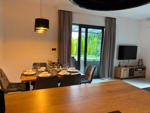 A dining area with a table set for four, a television on the wall, and a sliding glass door leading to a garden. - VISTA—a spacious 3-story apartment on the slopes of Karpacz; pets welcome (Województwo dolnośląskie)