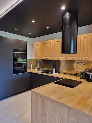 A modern kitchen with a built-in oven, a stainless steel range hood, wooden cabinets, a black sink, and a wooden countertop. - VISTA—a spacious 3-story apartment on the slopes of Karpacz; pets welcome (Województwo dolnośląskie)