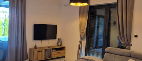 Ett modernt vardagsrum med en soffa, ett soffbord, en tv och ett stort fönster med gardiner.