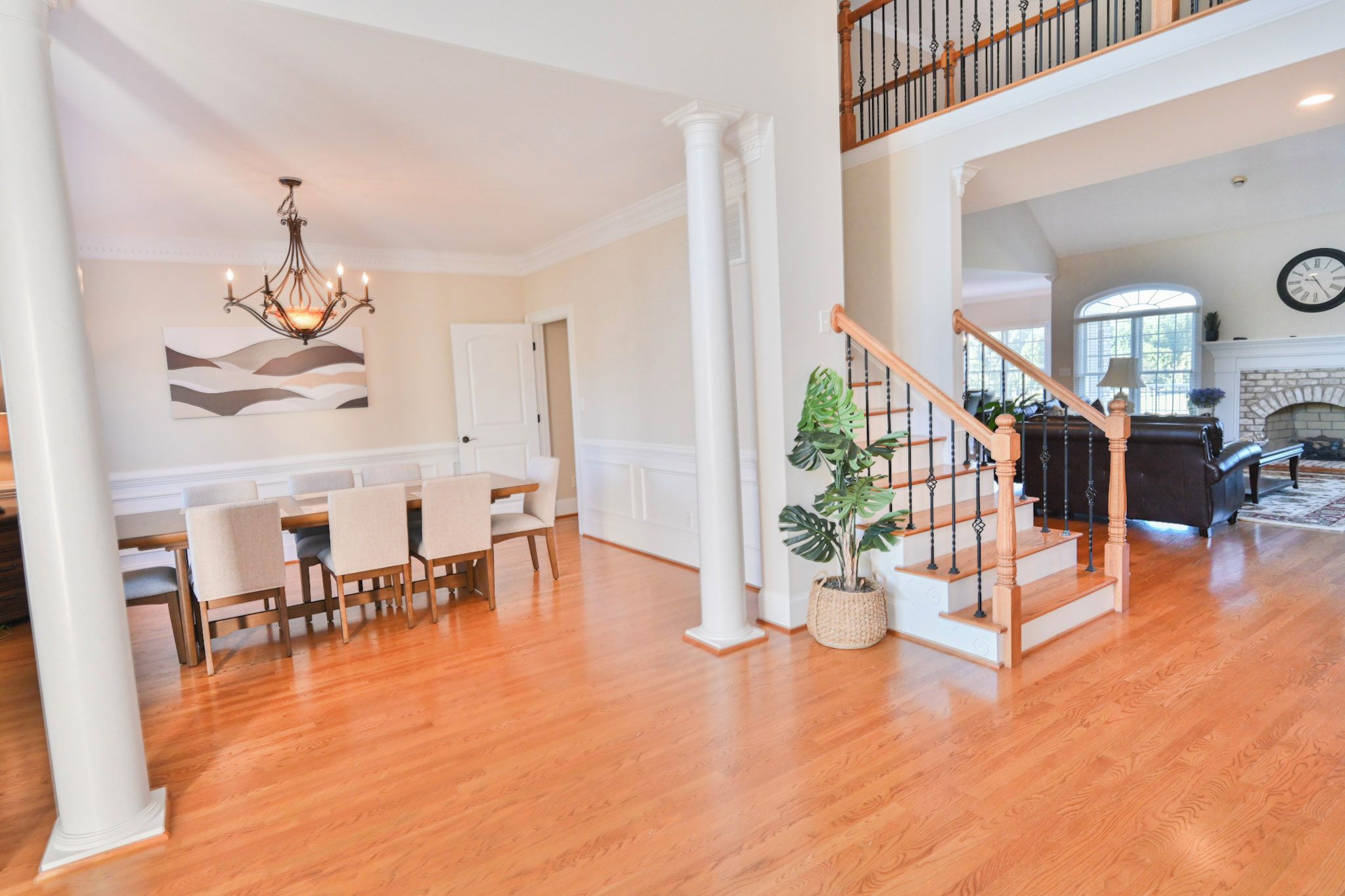 A spacious living area with a wooden staircase, a dining table with chairs, and a large potted plant.