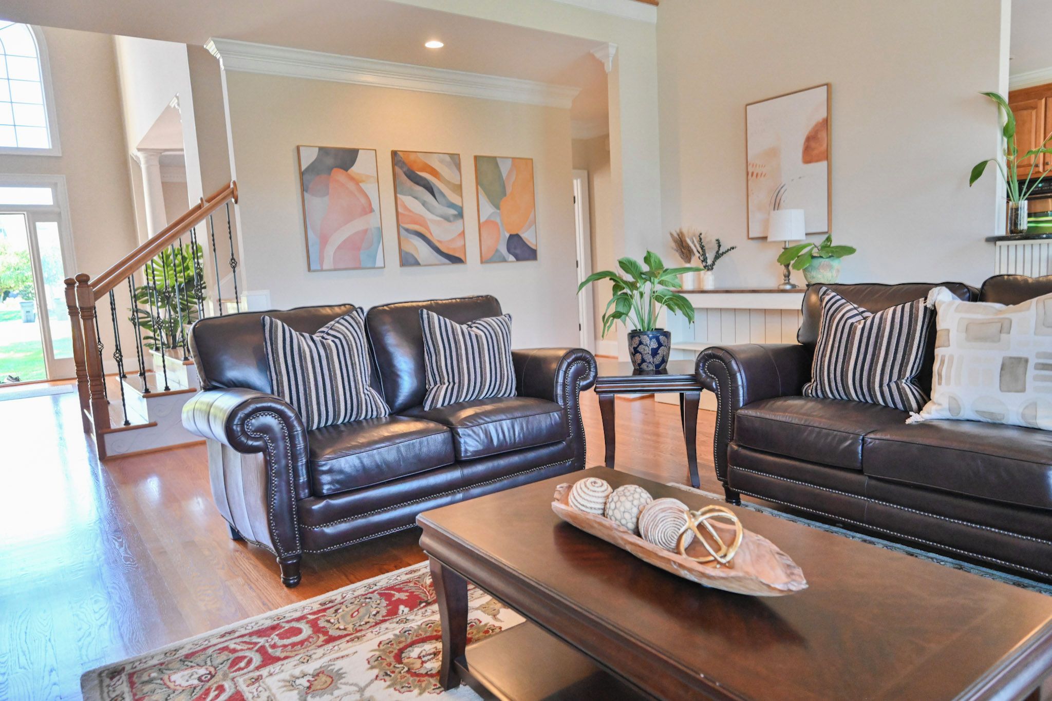 A living room with two black leather sofas, a coffee table with decorative items, and a staircase leading to another level.