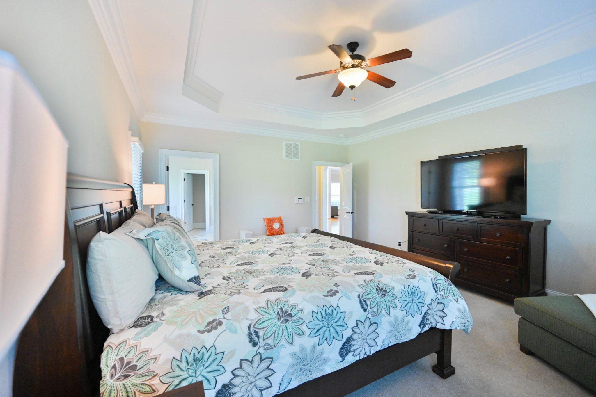 A bedroom with a bed, a television, a dresser, and a ceiling fan.