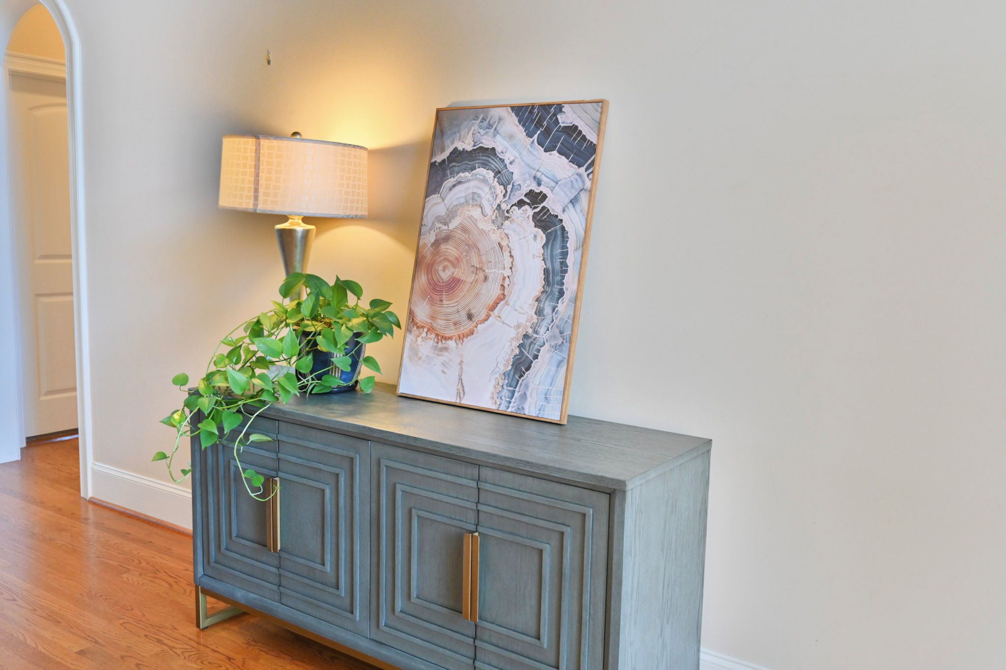 A hallway with a grey cabinet, a lamp, and a framed abstract artwork.