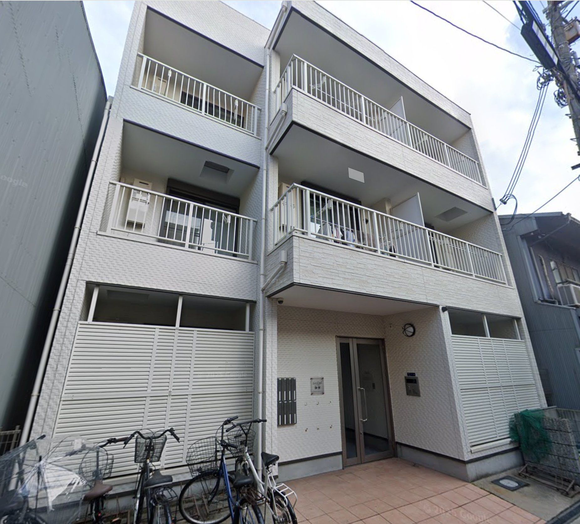 Un edificio residencial de varios pisos con balcones, una entrada con reja y bicicletas estacionadas afuera.