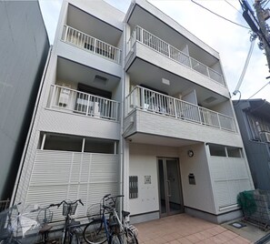 A multi-story residential building with balconies, a gated entrance, and bicycles parked outside. - HANASTAY MITSUHA & SEIRAN (Osaka)